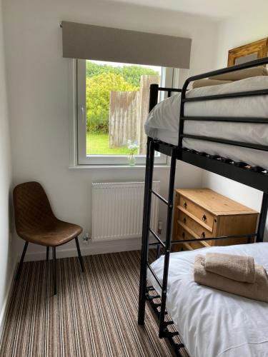 a bedroom with a bunk bed and a chair and a window at Wheal Rock - Luxury 2 Bed Lodge in St. Agnes