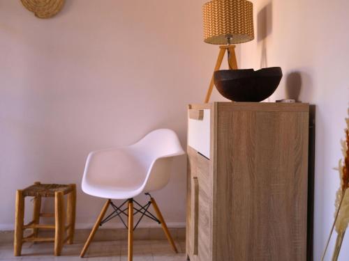 a room with a white chair and a lamp on a cabinet at L'Hacienda Joud - Privatisation de 5 chambres dans un havre de paix à Marrakech avec piscine & cuisinière privée dans le désert d'Aït Ourir in Aïn er Rmel