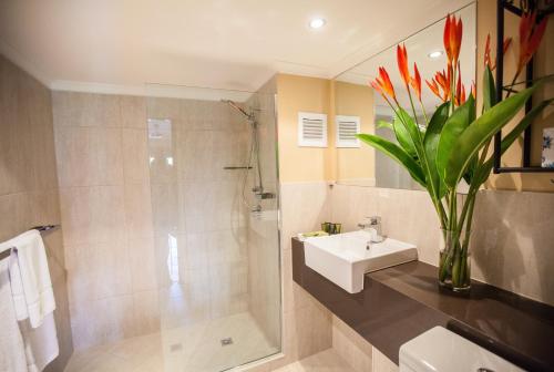 a bathroom with a sink and a shower and a vase of flowers at Villa San Michele (Official) in Port Douglas