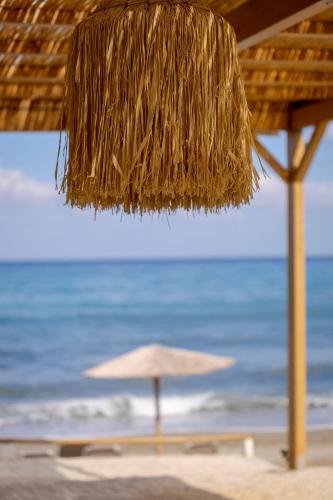 a straw umbrella on a beach with the ocean at Odysseus Aparthotel in Plataniás