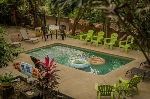 a swimming pool with green chairs and a table and a table and chairs at Casa Pura Vida Surf Hostel - Tamarindo Costa Rica in Tamarindo