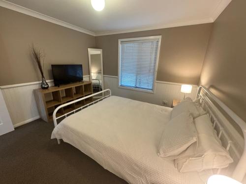 a bedroom with a white bed and a television at Singleton Rose Cottages in Singleton