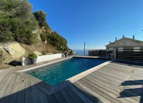 une piscine avec une terrasse en bois et une maison dans l'établissement Haut de villa avec piscine au bord de mer, à San-Martino-di-Lota