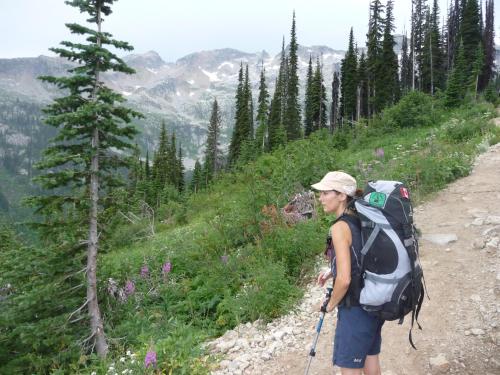 a woman with a backpack standing on a mountain trail at Fresh Studio Apartment in Central Rossland in Rossland