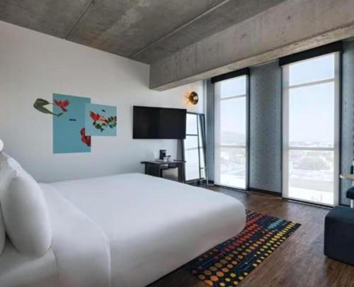 a bedroom with a large white bed and large windows at Aloft Guadalajara Sur in Guadalajara