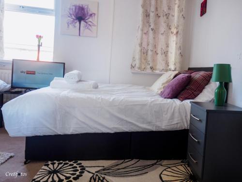 a bedroom with a bed with white sheets and a television at WoodHus Lodge Fantastic Large Double Room 3 in Stoke on Trent