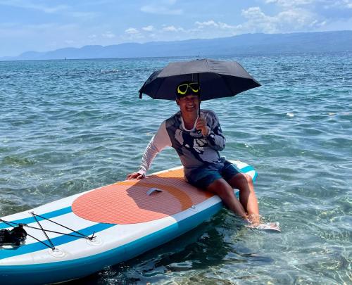a man sitting on a surfboard in the water with an umbrella at Boochee Beach in Tampi