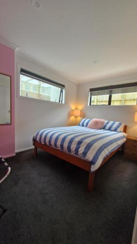 a bedroom with a bed with a striped comforter and two windows at Modern 2 BDRM Oakura Basement apartment in Oakura