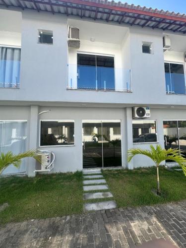 une maison blanche avec des portes en verre et des palmiers dans l'établissement Casa de Praia com piscina, à Santa Cruz Cabrália