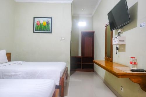 a room with two beds and a desk and a television at Joglo Manggisan Syariah Kotagede Mitra RedDoorz in Yogyakarta