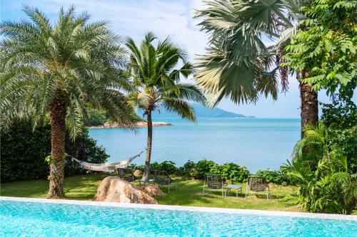 a pool with palm trees and a hammock and the ocean at Villa Maliya in Plai Laem
