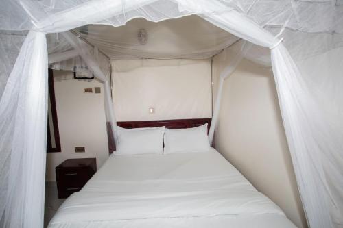 a bed in a small room with white curtains at Novella Guesthouse in Arua