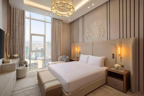 a bedroom with a white bed and a large window at Hilton Bahrain City Centre Hotel & Residences in Manama