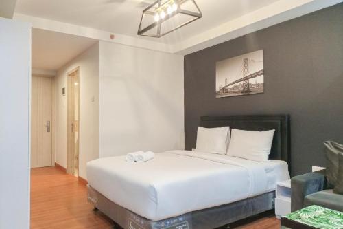 a bedroom with a large white bed and a chair at Cozy Studio at Mataram City Apartment By Travelio in Kejayan