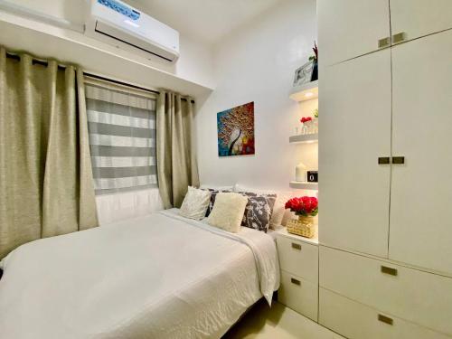 a white bedroom with a bed and a window at FameStaycation at FAME Residences in Manila