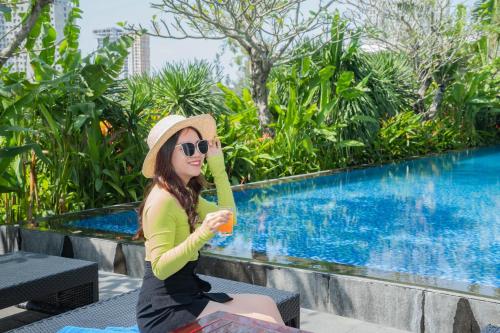 a woman in a hat sitting next to a swimming pool at Montgomerie Links Hotel & Villas in Hoi An
