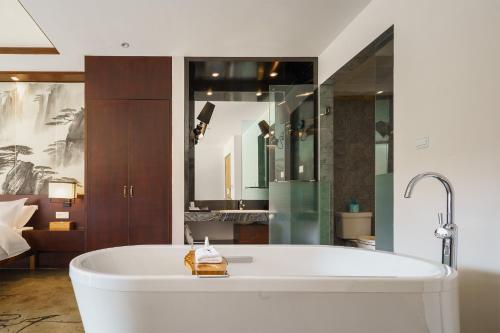 a large white tub in a room with a bedroom at Huangshan Shanshuijian Wei Boutique Hotel in Huangshan