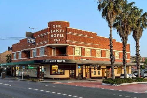 a building on a street with palm trees in front of it at The Lakes Hotel, Rosebery in Sydney