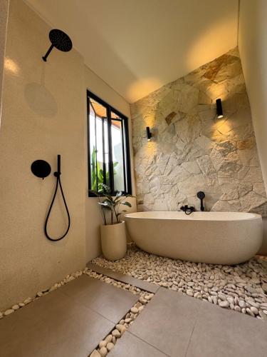 a bathroom with a tub and a stone wall at Romansa villa in Ubud