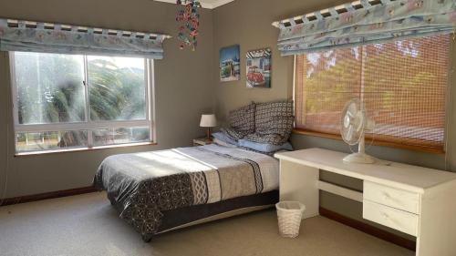 a bedroom with a bed and a desk and two windows at Sunset Retreat in Cape Town