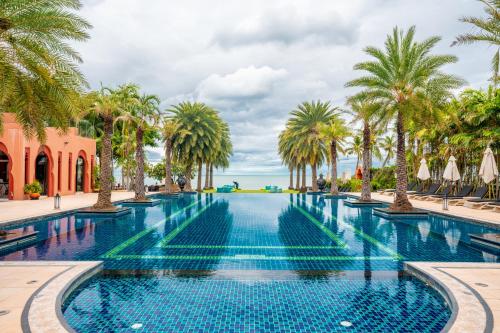 a swimming pool with palm trees and umbrellas at Marrakesh Hua Hin Resort & Spa in Hua Hin