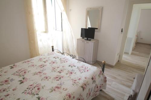 a bedroom with a bed with a floral bedspread and a television at Perla in Marina di Mancaversa