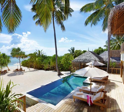 a pool with chairs and umbrellas next to a beach at Six Senses Laamu in Laamu