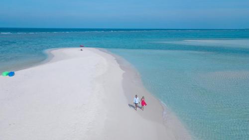two people walking on a white beach in the ocean at Arista Villa in Ukulhas