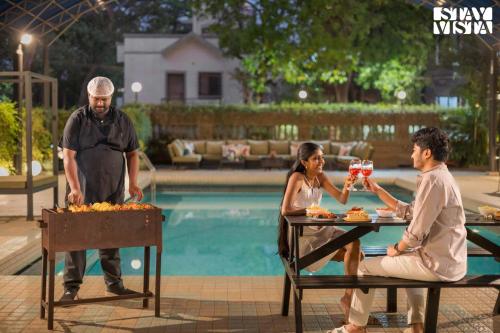 a man and a woman sitting at a table near a pool at Mehta Mansion by StayVista - A Villa with a Swimming Pool and Pool Table in Lonavala