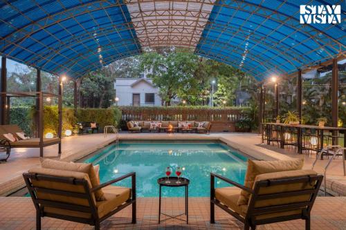 a swimming pool with chairs and a blue roof at Mehta Mansion by StayVista - A Villa with a Swimming Pool and Pool Table in Lonavala