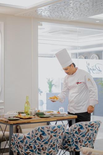 a chef standing in a kitchen holding a plate of food at Royal Prime - A City Center Boutique Hotel In Jaipur in Jaipur