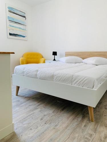 - un lit blanc dans une chambre avec une chaise jaune dans l'établissement Appart - central - Cœur historique, à Sarlat-la-Canéda