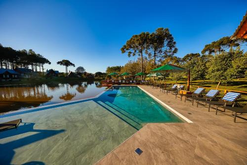a swimming pool with chairs and umbrellas next to a lake at Hospedaria Morada das Grimpas in Palmeira