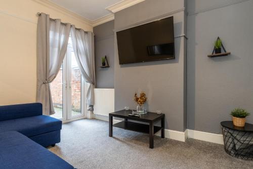 a living room with a blue couch and a tv on the wall at Beacon House in Leicester