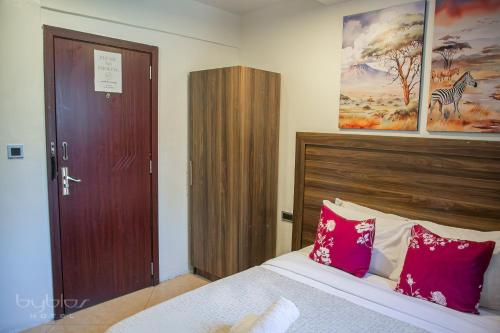 a bedroom with a bed with pink pillows and a wooden door at Byblos Hotel-Sky Osu in Accra