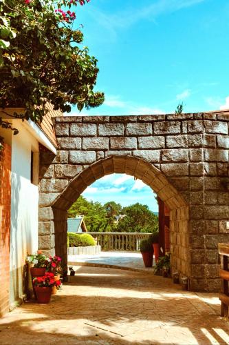 an archway in a stone wall with flowers in a yard at Pousada Recanto dos Sonhos in Campos do Jordão