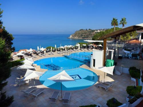 a swimming pool with umbrellas and chairs and the ocean at Hotel Village Scoglio Della Galea in Capo Vaticano