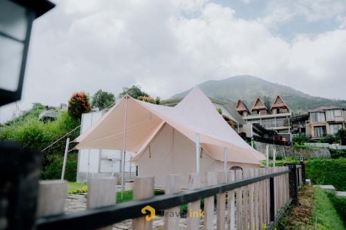 a building with a pointed roof in front of a town at Glamping Telaga Menjer By Travelink in Kejajar