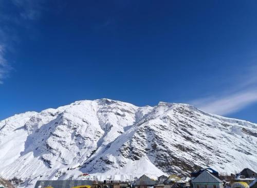 a snow covered mountain with houses in front of it at Rupi Rani Home Stay in Gushāl