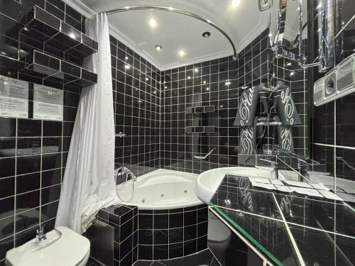 a black tiled bathroom with a tub and a toilet at Hotel Plata in Ibi
