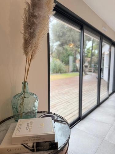 a vase on a glass table with a book and a book at La Villa Pinède avec SPA à 5 minutes de la mer in Brétignolles-sur-Mer
