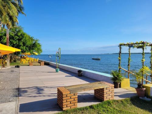 a bench on a sidewalk next to the water at Apartamento Ilha Cacha Pregos, Vera Cruz in Vera Cruz de Itaparica