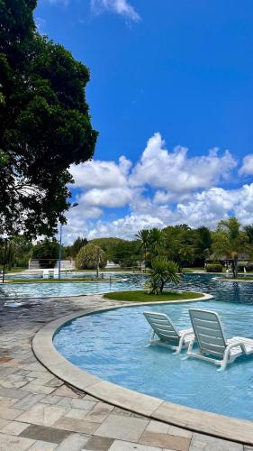 two white chairs sitting in a swimming pool at Apartamento no Iloa Residence - Com Enxoval Completo in Barra de São Miguel