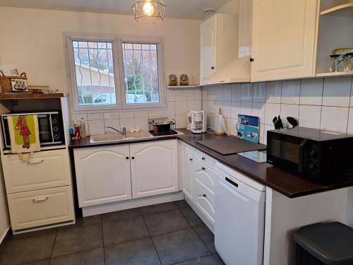 une cuisine avec des armoires blanches et un micro-ondes dans l'établissement Loue charmante petite maison dans un écrin de verdure, à Saint-Vivien-de-Médoc