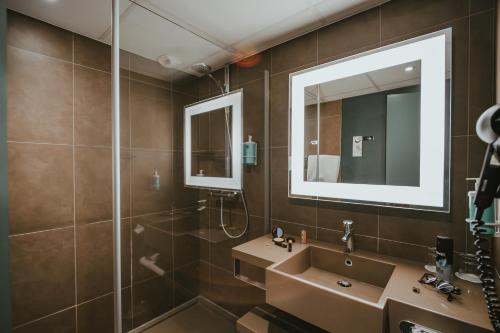une salle de bain avec un lavabo et une douche avec un miroir dans l'établissement Novotel Lens Noyelles, à Noyelles-Godault