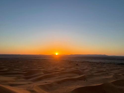 a sunset in the desert with the sun setting at Hotel Les Roches Merzouga in Merzouga