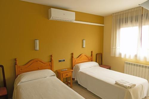 two beds in a room with yellow walls at HOSTAL La MARAVILLOSA DE VALDERAS in Valderas