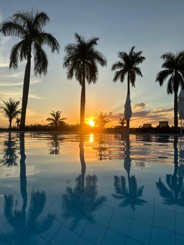 a pool with palm trees in front of a sunset at Riviera Santa Cristina l in Arandu