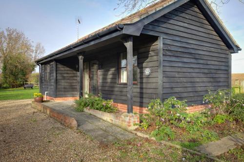 a small black house with a porch and some plants at Fushia Chalet a lovely little rural retreat in Saxtead