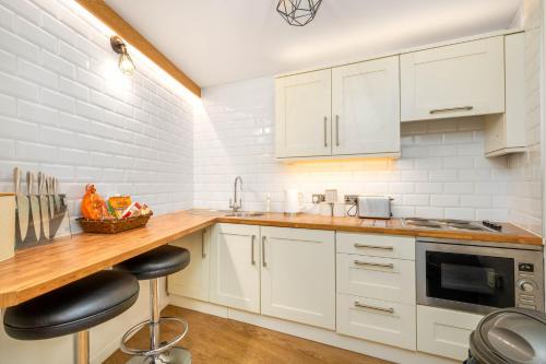 a kitchen with white cabinets and a counter with stools at Chunal Apartment Central Glossop in Glossop